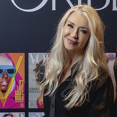 Session Stylistin Nicci Welsh posiert vor einer Fotowand mit Covern von Modemagazinen, die Oribe gestylt hat